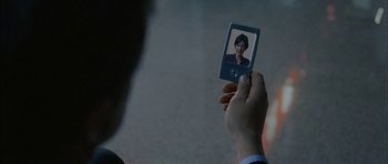 Movie still from “Code 46” (2003), directed by Michael Winterbottom – A person holding a cell phone up to their face; Extreme Close Up shot, Over the shoulder angle