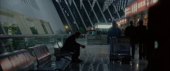 Movie still from “Code 46” (2003), directed by Michael Winterbottom – A man sitting on a bench in an airport terminal; Wide shot, High angle