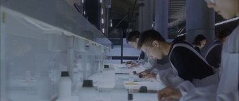 Movie still from “Code 46” (2003), directed by Michael Winterbottom – A group of people sitting at a table with a cell phone; Medium shot, High angle