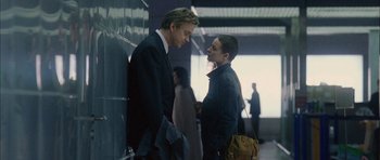 Movie still from “Code 46” (2003), directed by Michael Winterbottom – Two men in business suits talking to each other; Medium shot, Over the shoulder angle