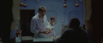 Movie still from “Code 46” (2003), directed by Michael Winterbottom – A man and a woman standing in front of a table; Medium shot, High angle