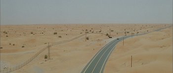 Movie still from “Code 46” (2003), directed by Michael Winterbottom – An aerial view of an empty road in the middle of the desert; Extreme Wide shot, High angle