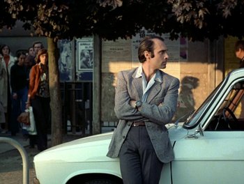 Movie still from “Cousin cousine” (1975), directed by Jean-Charles Tacchella – A man standing next to a car on the side of the road; Medium shot, Low angle