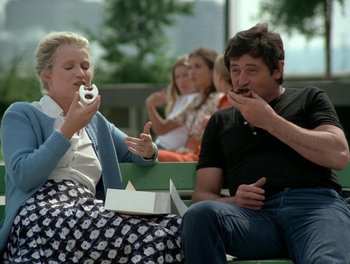 Movie still from “Cousin cousine” (1975), directed by Jean-Charles Tacchella – A man and a woman sitting on a bench eating a donut; Medium shot, Low angle