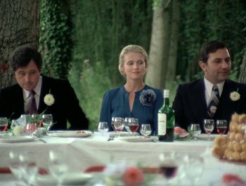 Movie still from “Cousin cousine” (1975), directed by Jean-Charles Tacchella – A woman sitting at a table with two other people; Medium shot, Over the shoulder angle