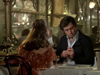 Movie still from “Cousin cousine” (1975), directed by Jean-Charles Tacchella – A man and a woman sitting at a table in front of a cell phone; Medium shot, Over the shoulder angle
