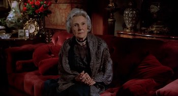 Movie still from “Family Plot” (1976), directed by Alfred Hitchcock – An older woman sitting on a red couch in a living room; Medium shot, Low angle