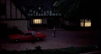 Movie still from “Family Plot” (1976), directed by Alfred Hitchcock – A man and a woman standing in front of a red car; Extreme Wide shot, High angle