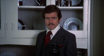 Movie still from “Family Plot” (1976), directed by Alfred Hitchcock – A man in a suit and tie standing in front of a shelf; Close Up shot, Low angle