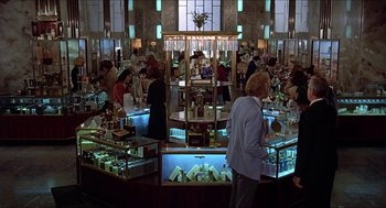 Movie still from “Family Plot” (1976), directed by Alfred Hitchcock – A group of people standing in a room with a display case; Wide shot, Low angle