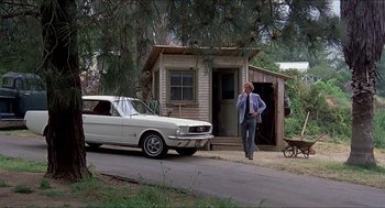 Movie still from “Family Plot” (1976), directed by Alfred Hitchcock – A man standing next to a white car on the side of the road; Wide shot, Low angle