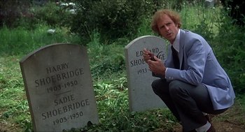 Movie still from “Family Plot” (1976), directed by Alfred Hitchcock – A man kneeling next to two headstones in a cemetery; Close Up shot, Over the shoulder angle