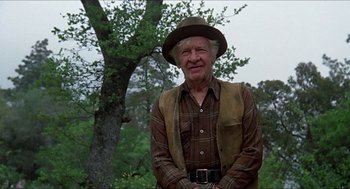 Movie still from “Family Plot” (1976), directed by Alfred Hitchcock – An older man wearing a hat standing in front of a tree; Medium shot, Low angle