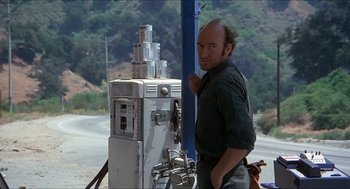 Movie still from “Family Plot” (1976), directed by Alfred Hitchcock – A man standing next to an old gas pump on the side of the road; Medium shot, Over the shoulder angle
