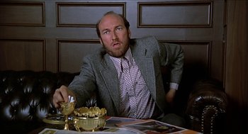 Movie still from “Family Plot” (1976), directed by Alfred Hitchcock – A man sitting in front of a table with a bowl of food; Close Up shot, Low angle