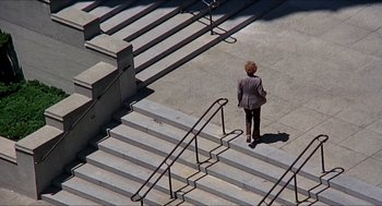 Movie still from “Family Plot” (1976), directed by Alfred Hitchcock – A woman walking up some stairs in a suit; Extreme Wide shot, High angle