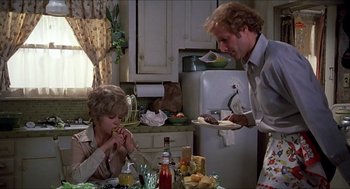 Movie still from “Family Plot” (1976), directed by Alfred Hitchcock – A man and a woman in a kitchen eating food; Medium shot, High angle