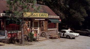 Movie still from “Family Plot” (1976), directed by Alfred Hitchcock – An old fashioned coffee shop with a car parked in front of it; Wide shot, High angle