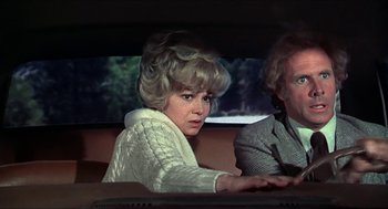 Movie still from “Family Plot” (1976), directed by Alfred Hitchcock – A woman sitting in the back seat of a car next to a man; Medium shot, Over the shoulder angle