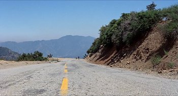 Movie still from “Family Plot” (1976), directed by Alfred Hitchcock – Two bicyclists riding down a road near a mountain; Extreme Wide shot, High angle