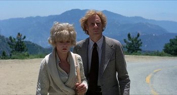 Movie still from “Family Plot” (1976), directed by Alfred Hitchcock – A man and a woman standing next to each other on a dirt road; Medium shot, Low angle