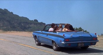 Movie still from “Family Plot” (1976), directed by Alfred Hitchcock – A group of people riding in the back of a blue car on a road; Wide shot, Low angle