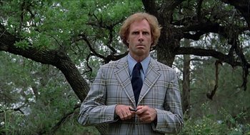 Movie still from “Family Plot” (1976), directed by Alfred Hitchcock – A man in a plaid jacket and tie standing in front of a tree; Medium shot, Low angle