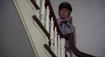 Movie still from “Family Plot” (1976), directed by Alfred Hitchcock – A man wearing a hat standing at the top of a staircase; Medium shot, Low angle