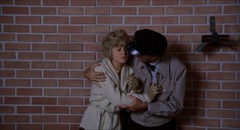 Movie still from “Family Plot” (1976), directed by Alfred Hitchcock – A man and a woman hugging in front of a brick wall; Medium shot, Low angle