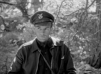 Movie still from “Fear and Desire” (1952), directed by Stanley Kubrick – A man in a military uniform is standing in front of a tree; Medium shot, High angle