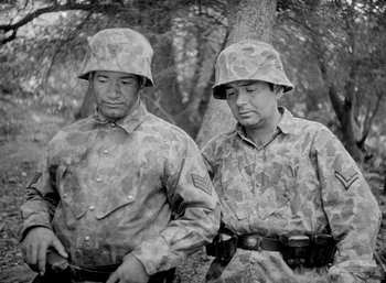 Movie still from “Fear and Desire” (1952), directed by Stanley Kubrick – Two men in military uniforms standing next to a tree; Medium shot, Low angle