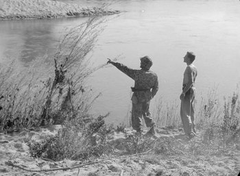 Movie still from “Fear and Desire” (1952), directed by Stanley Kubrick – Two men standing next to a body of water; Wide shot, High angle