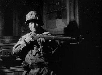Movie still from “Fear and Desire” (1952), directed by Stanley Kubrick – An old photo of a man holding a rifle; Medium shot, Low angle