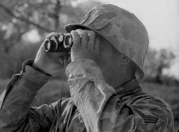Movie still from “Fear and Desire” (1952), directed by Stanley Kubrick – A soldier looking through binoculars while standing in a field; Close Up shot, Over the shoulder angle