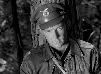 Movie still from “Fear and Desire” (1952), directed by Stanley Kubrick – A man in a military uniform is leaning against a tree; Medium shot, High angle