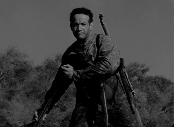 Movie still from “Fear and Desire” (1952), directed by Stanley Kubrick – Black and white photograph of a man holding a rifle; Medium shot, Low angle