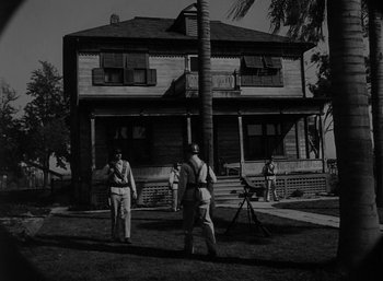 Movie still from “Fear and Desire” (1952), directed by Stanley Kubrick – A black - and - white photo of two men standing in front of a house; Wide shot, Low angle
