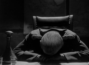 Movie still from “Fear and Desire” (1952), directed by Stanley Kubrick – A man sitting at a table with his head on his hands; Medium shot, High angle