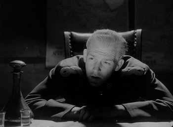 Movie still from “Fear and Desire” (1952), directed by Stanley Kubrick – An older man sitting at a table in a room; Close Up shot, Low angle