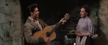 Movie still from “Flaming Star” (1960), directed by Don Siegel – A man holding a guitar in front of another man; Medium shot, Over the shoulder angle