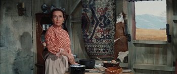 Movie still from “Flaming Star” (1960), directed by Don Siegel – A woman standing in front of a table filled with food; Medium shot, High angle