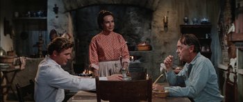 Movie still from “Flaming Star” (1960), directed by Don Siegel – A woman standing in front of a table with food on top of it; Medium shot, Over the shoulder angle