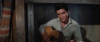 Movie still from “Flaming Star” (1960), directed by Don Siegel – A man holding a guitar while wearing a shirt; Close Up shot, Low angle