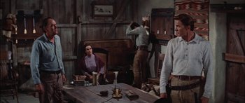 Movie still from “Flaming Star” (1960), directed by Don Siegel – A group of people standing around a wooden table; Medium shot, Over the shoulder angle