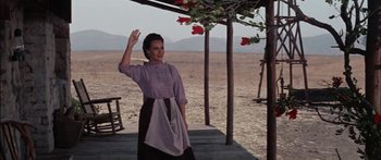 Movie still from “Flaming Star” (1960), directed by Don Siegel – An older woman standing on a porch waving; Wide shot, Low angle