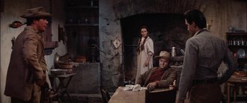 Movie still from “Flaming Star” (1960), directed by Don Siegel – A man and a woman sitting at a table in front of a fireplace; Medium shot, Over the shoulder angle