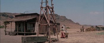 Movie still from “Flaming Star” (1960), directed by Don Siegel – An old west scene with a woman standing in front of a wooden structure; Extreme Wide shot, Low angle