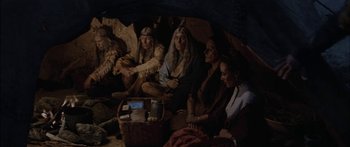 Movie still from “Flaming Star” (1960), directed by Don Siegel – A group of people sitting in a cave with a basket; Wide shot, High angle