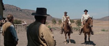 Movie still from “Flaming Star” (1960), directed by Don Siegel – A man riding a horse in a field with another man standing next to him; Wide shot, Over the shoulder angle