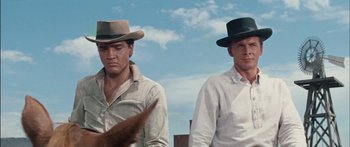 Movie still from “Flaming Star” (1960), directed by Don Siegel – A couple of men standing next to each other wearing hats; Medium shot, Low angle